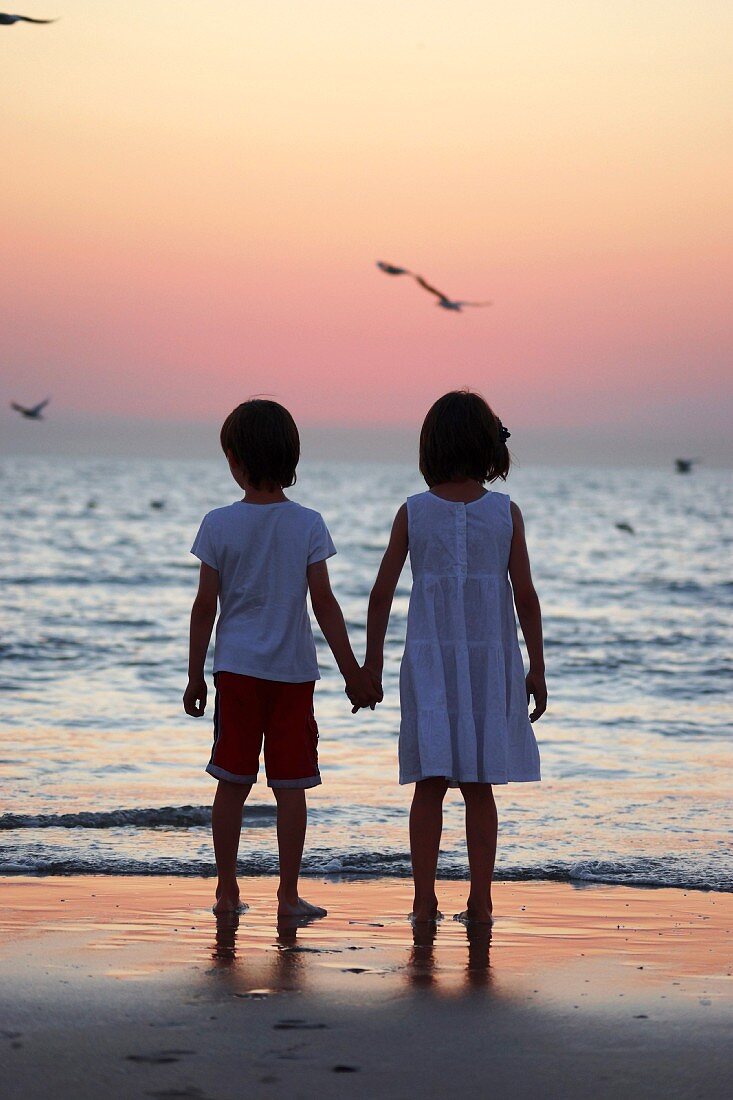 Junge und Mädchen Hand in Hand am Meeresufer in Abendstimmung
