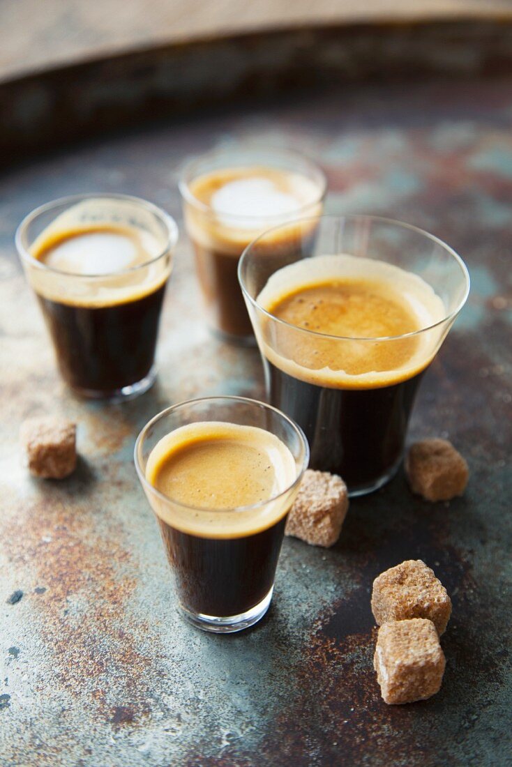 Various glasses of coffee with sugar cubes on a metal surface