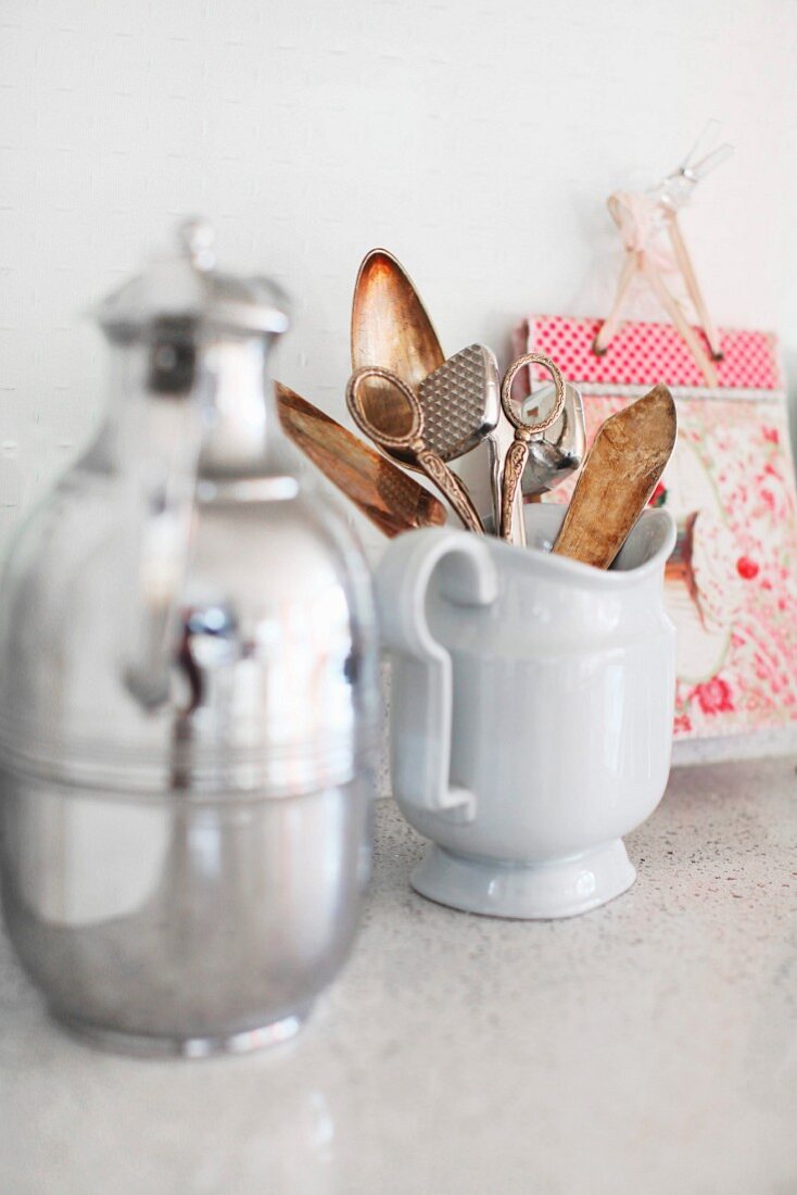 Thermos flask and china jug of kitchen utensils on stone surface