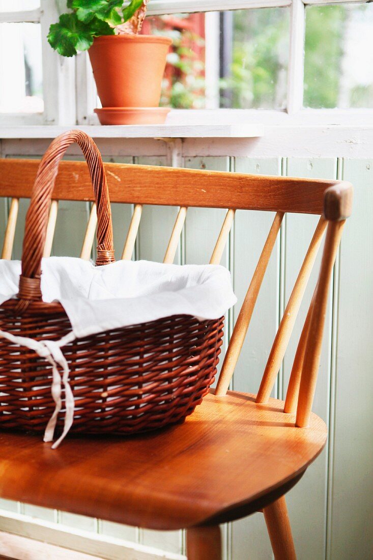 Handled basket lined with white cloth on 50s wooden bench in porch of Swedish wooden house
