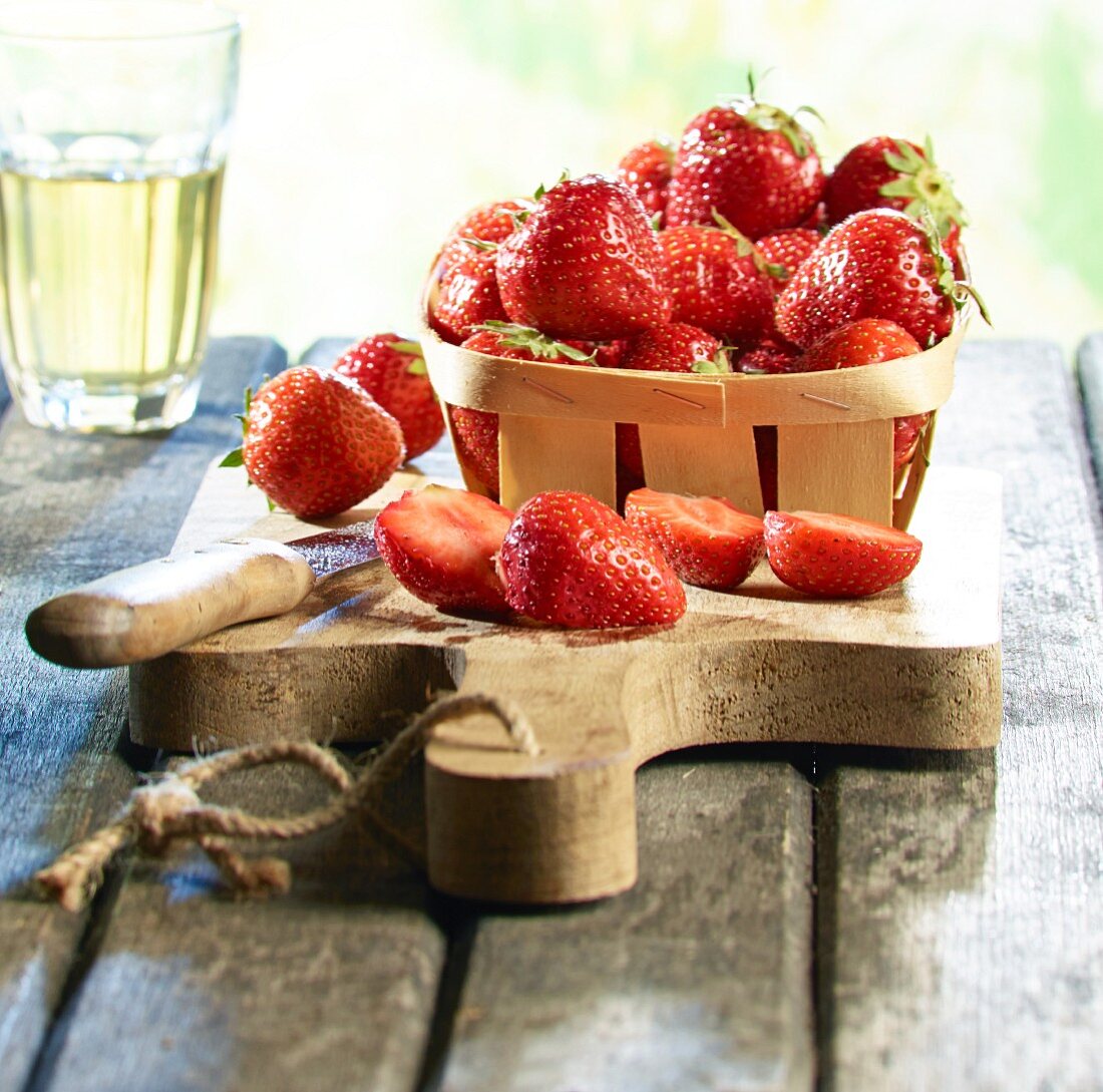 Fresh strawberries in a wooden basket on a chopping board with a knife