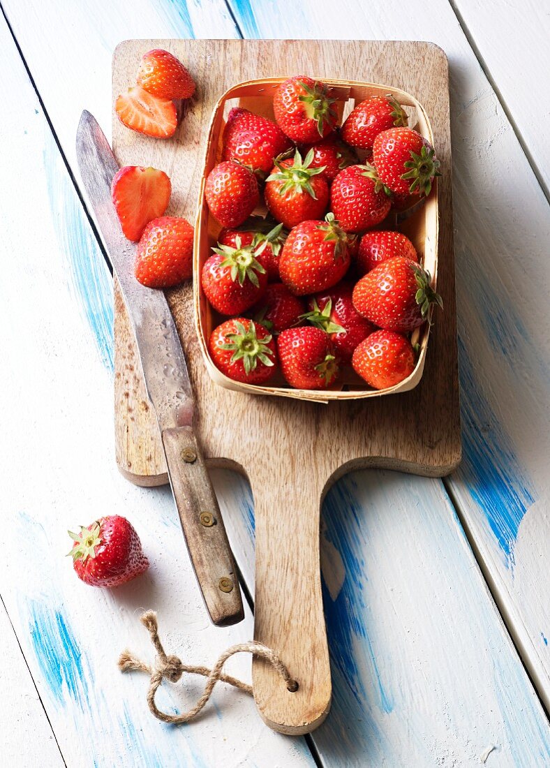 Fresh strawberries in a wooden basket on a chopping board with a knife