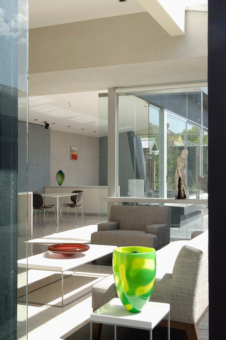 Open-plan interior with pale furniture and glass walls leading to terrace; dining area in background