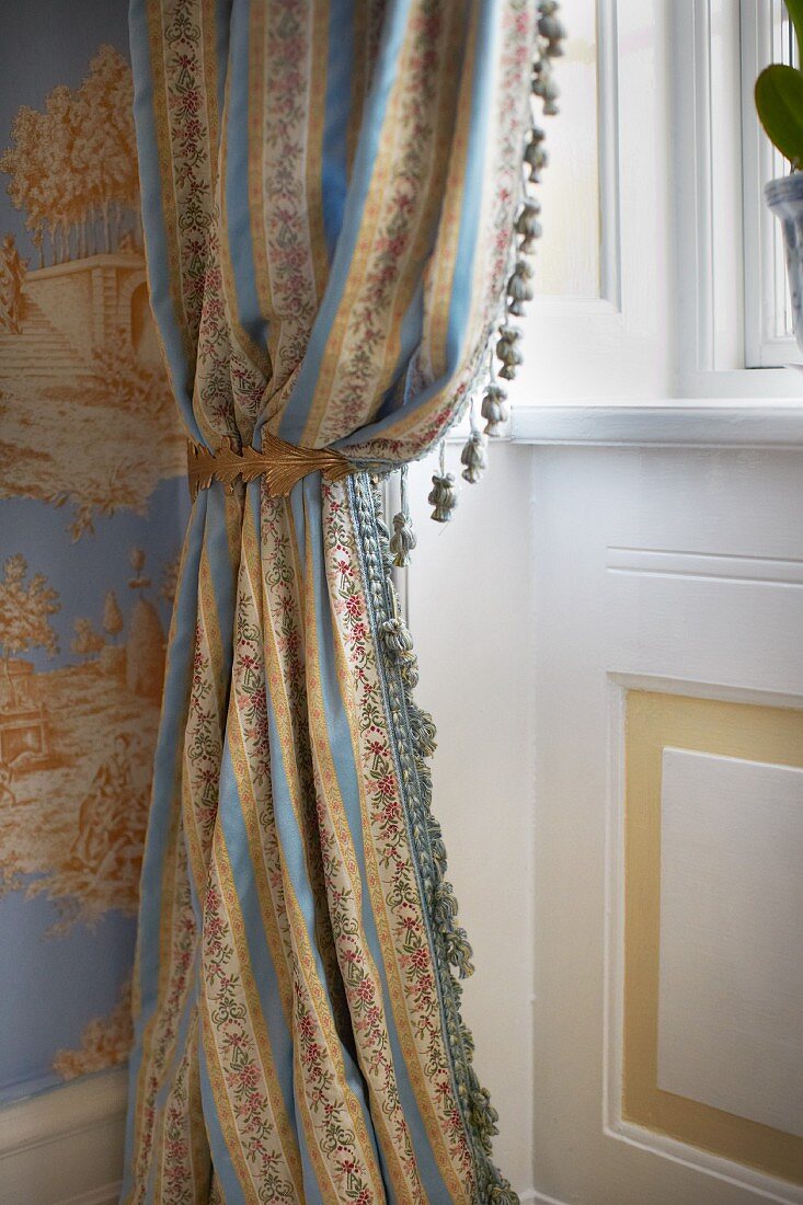 Draped curtain with small tassels in front of window in traditional, elegant interior