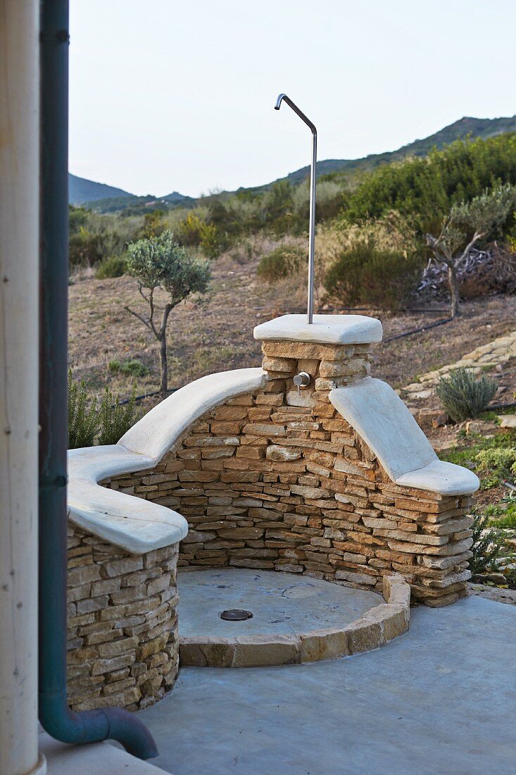 Outdoor shower with half-height stone wall in front of Mediterranean landscape