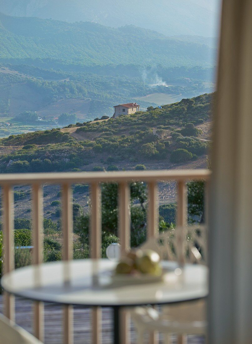 View through window across balcony to Mediterranean house in mountain landscape
