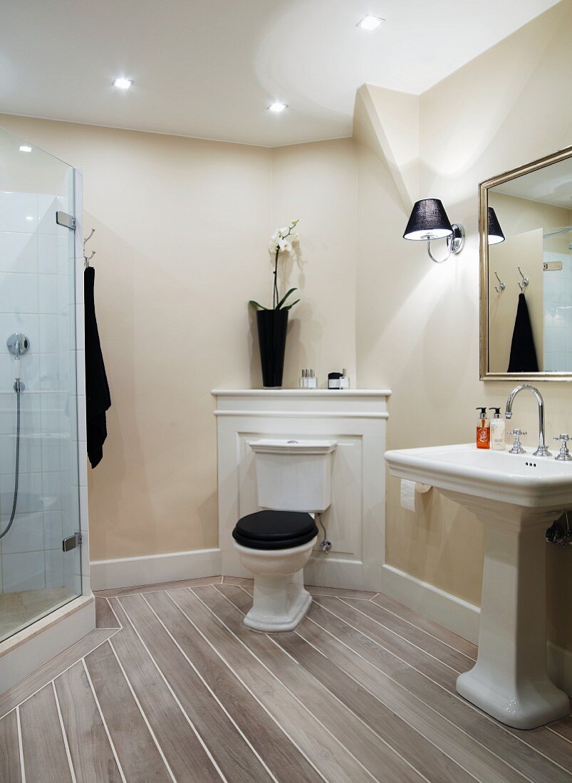 Traditional bathroom; pedestal toilet with cistern against wooden panel in corner, pedestal sink and modern glass shower cubicle