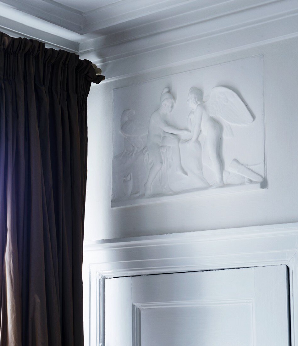 White, mythological low relief panel above traditional interior door with dark brown curtain to one side