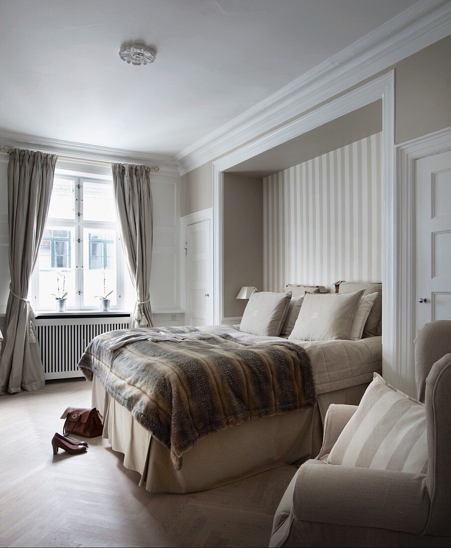 Bedspread and stacked pillows on box-spring bed in niche in traditional bedroom with subdued colour scheme