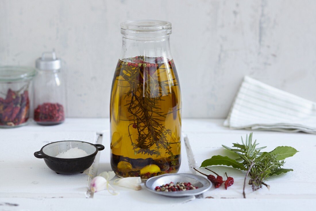 Homemade herb oil in a glass bottle surrounded by ingredients