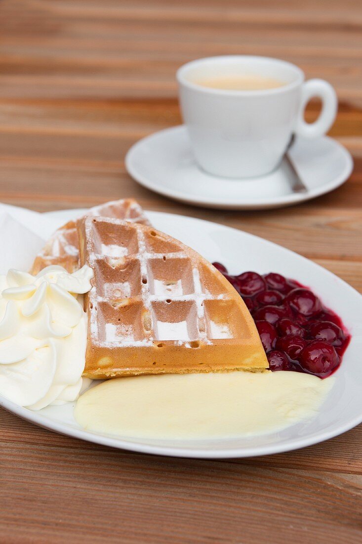 A Belgian waffle with cream, cherries and vanilla sauce