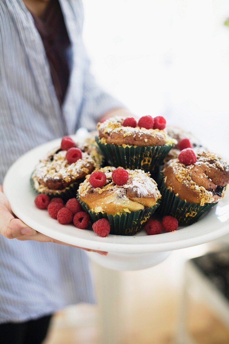 Person hält Schale mit Muffins und frischen Himbeeren