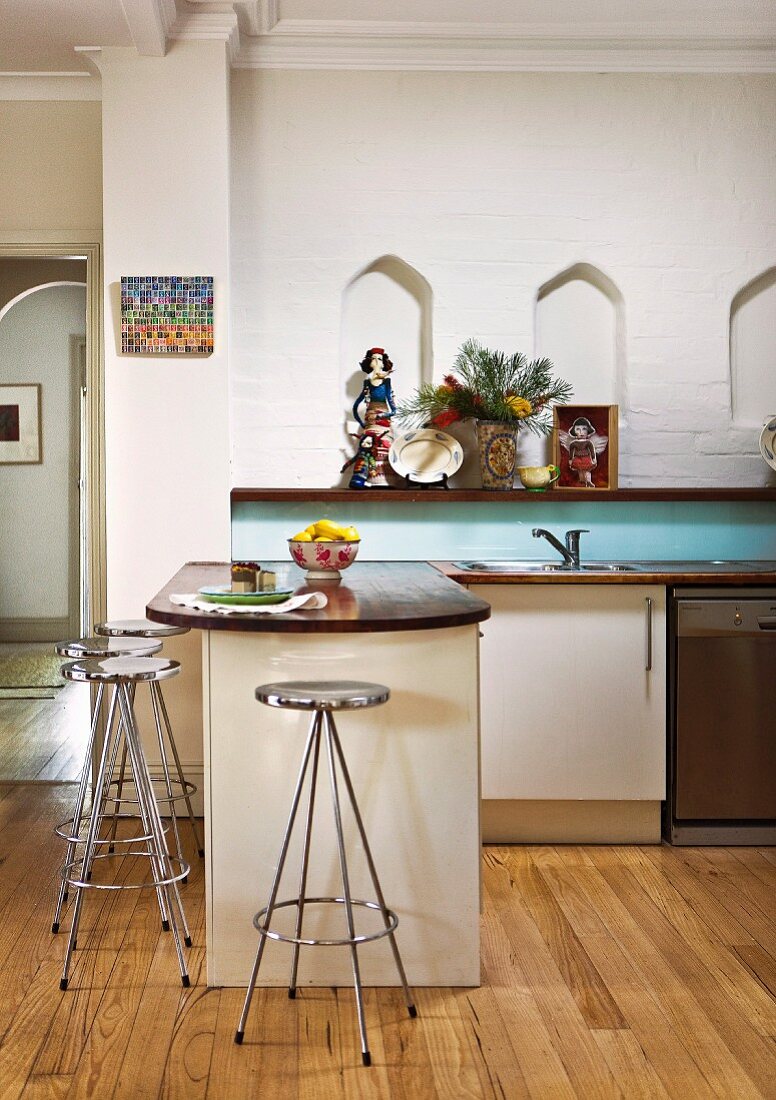 Retro chrome bar stools at kitchen counter on wooden floor, wooden shelf below small ogee niches in wall in background