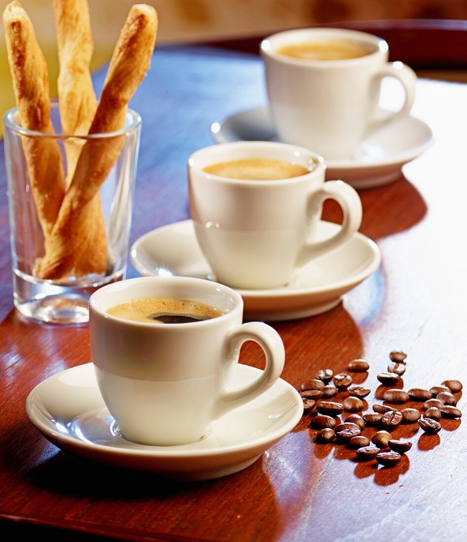 Three espressos, salted breadsticks and coffee beans on a table