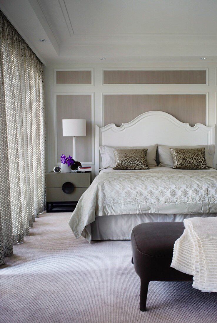 Double bed with curved, white-painted wooden headboard against wood-panelled wall with white frames in elegant bedroom