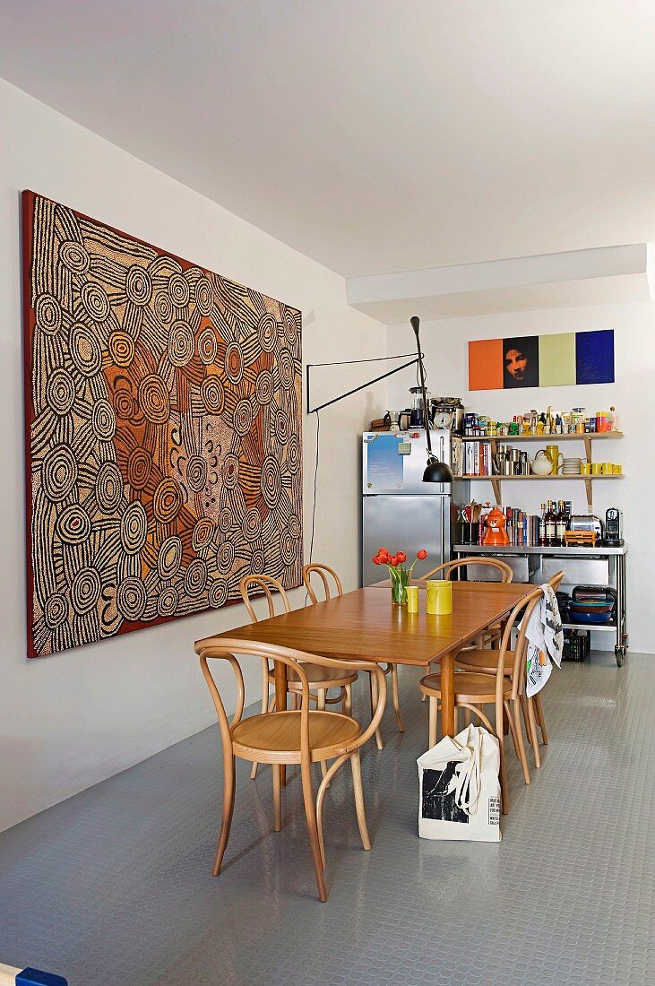 Large aboriginal artwork, dining table, bentwood chairs and colourful objects on kitchen shelves in background