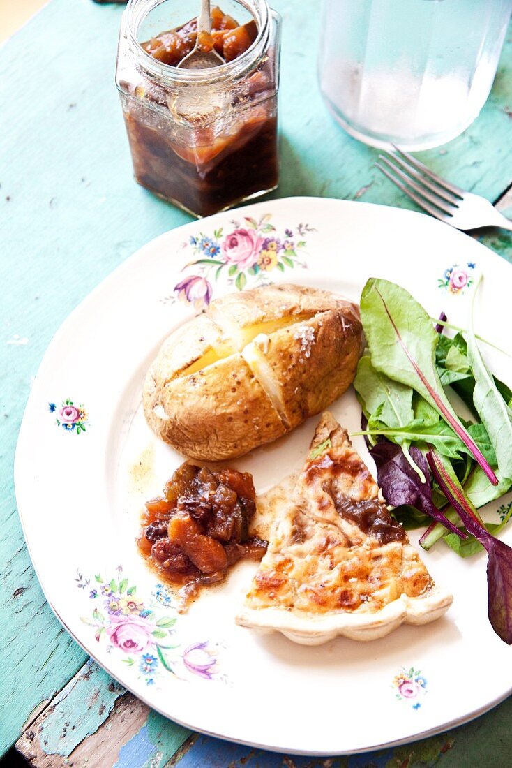 A slice of onion tart with a baked potato, salad and apple and courgette chutney