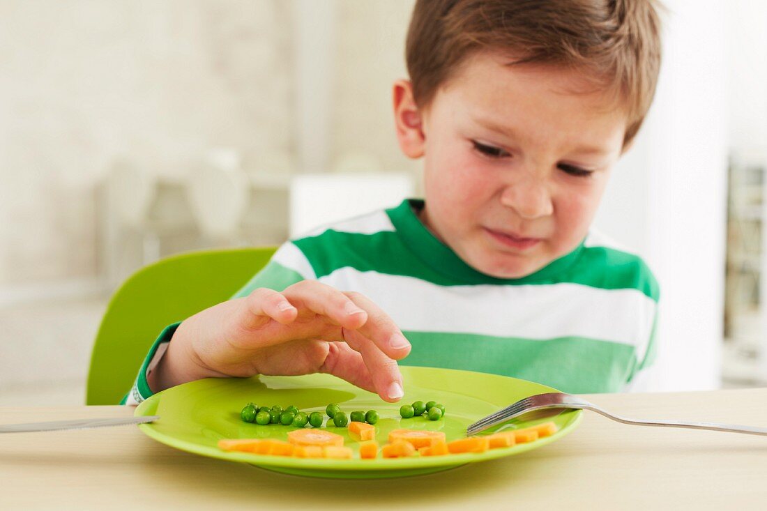 A little boy who doesn't want to eat peas and carrots