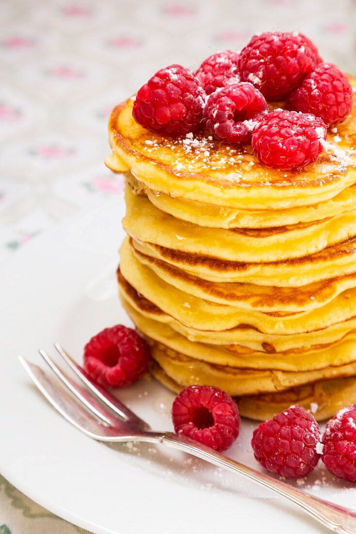 A stack of pancakes with honey, raspberries and icing sugar