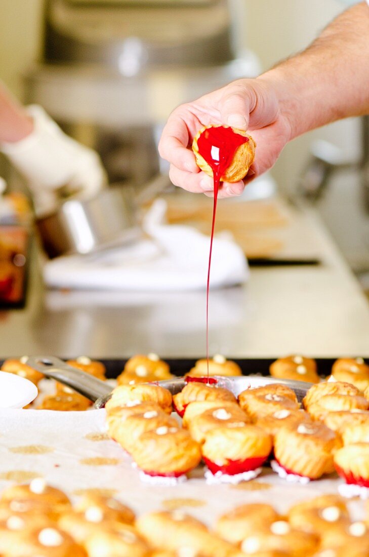 A confectioner dipping profiteroles into red caramel sauce (preparation for a croquembouche wedding cake, France)