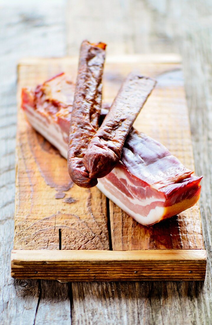 Geräucherte Schweinewürstchen auf einer Scheibe geräuchertem, gesalzenen Schweinefleisch (Frankreich)