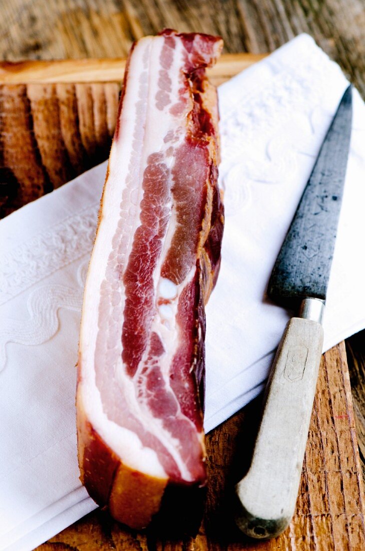 Geräucherter Schweinebauch aus Frankreich mit Messer auf Tuch