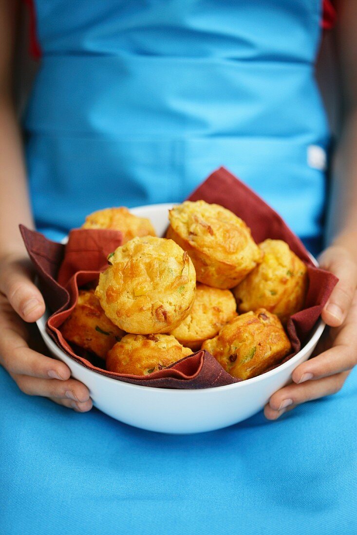 A child holding a bowl of cheese muffins