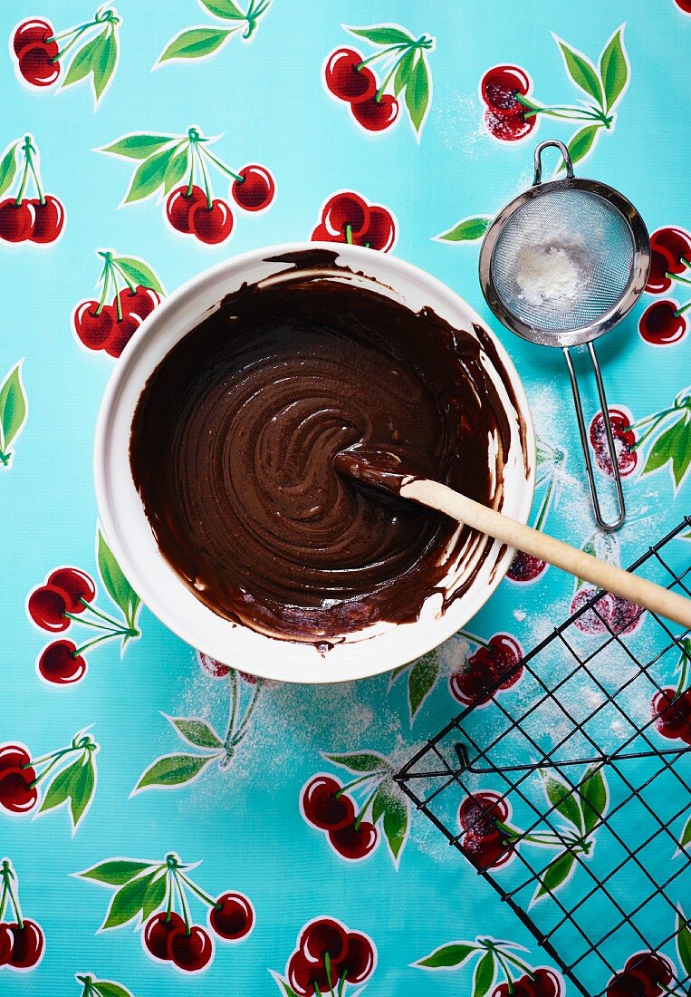 Chocolate cake mix in a bowl with a sieve and icing sugar
