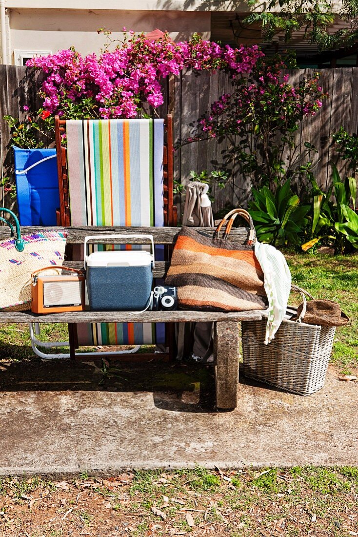 Verwitterte Gartenbank mit Strandtaschen in sommerlichem Garten