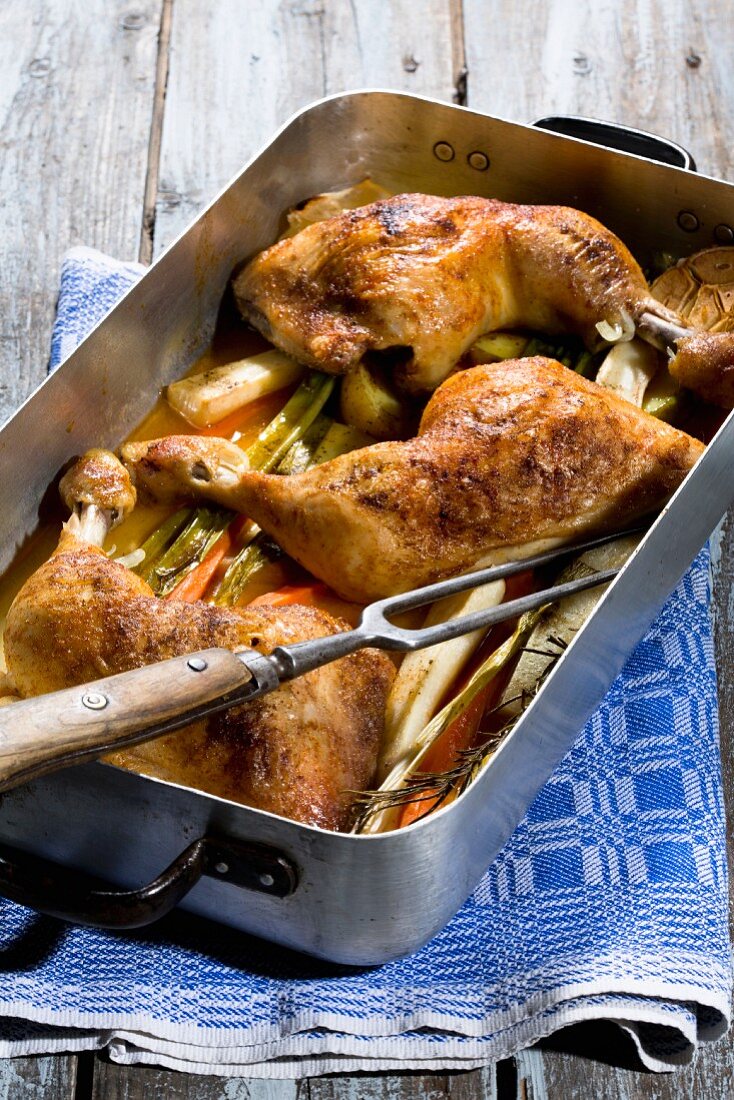 Chicken legs with root vegetables and lemons in a white wine sauce in a roasting tin