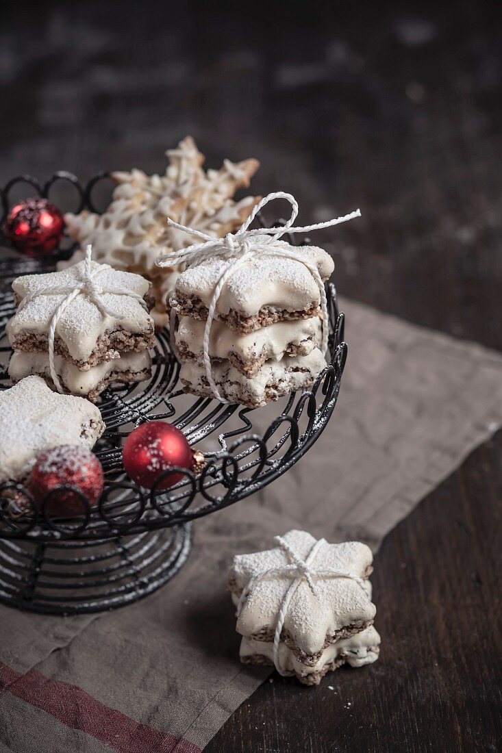Cinnamon stars decorated with icing sugar with red Christmas baubles on a cake stand