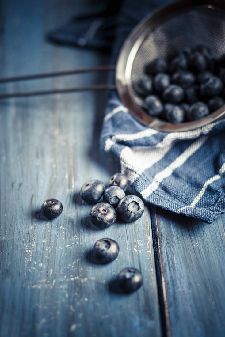 Heidelbeeren mit Sieb auf blauem Holztisch