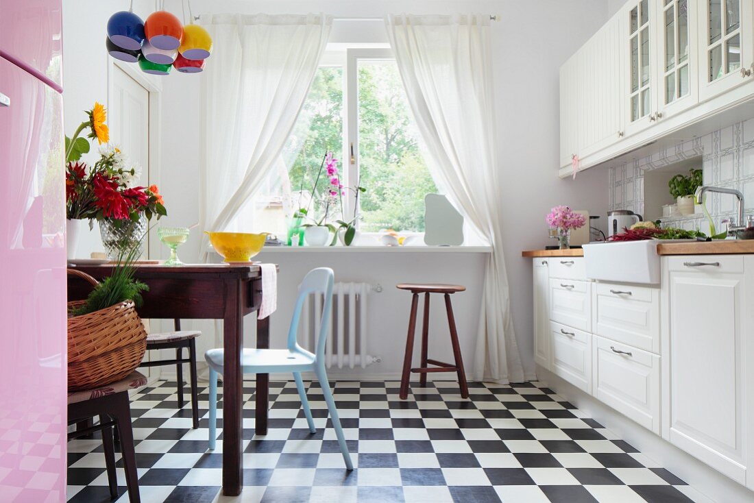 weiße Landhausküche mit schwarzweissem Schachbrettmusterboden, Essplatz mit altem Holztisch und Stühle im Retro Look