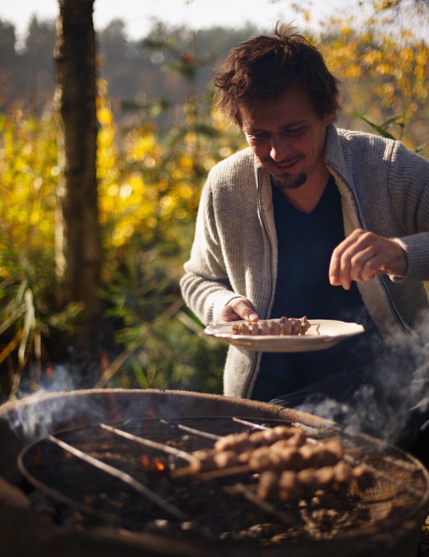 A man grilling venison skewers at an autumn picnic in a forest