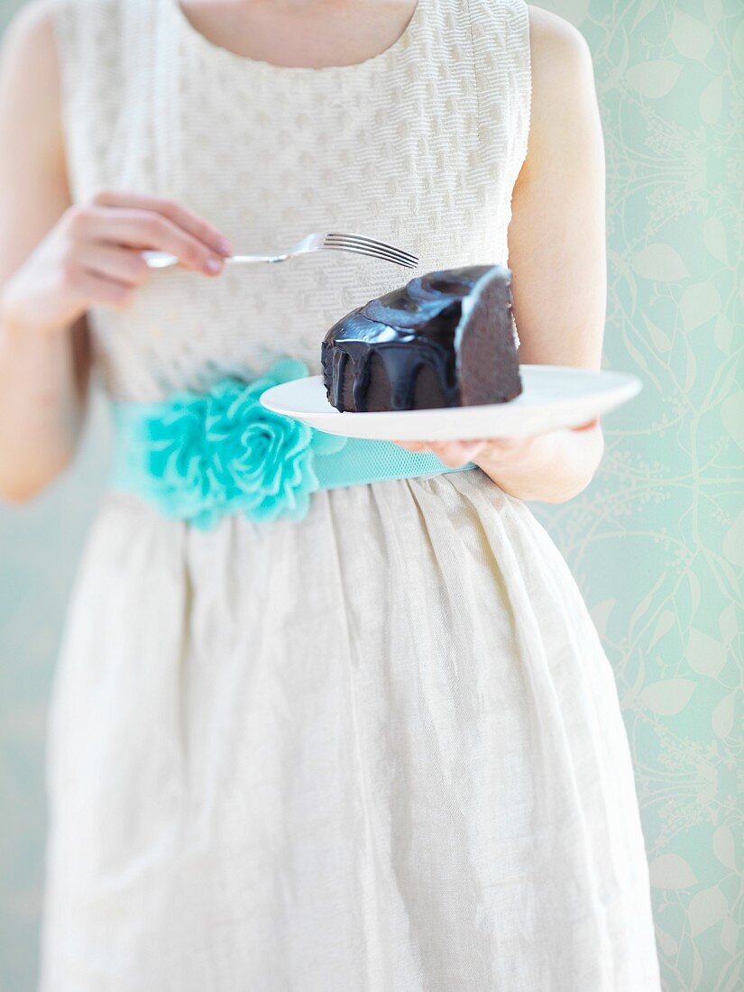 Frau in weißem Kleid isst ein Stück Schokoladenkuchen