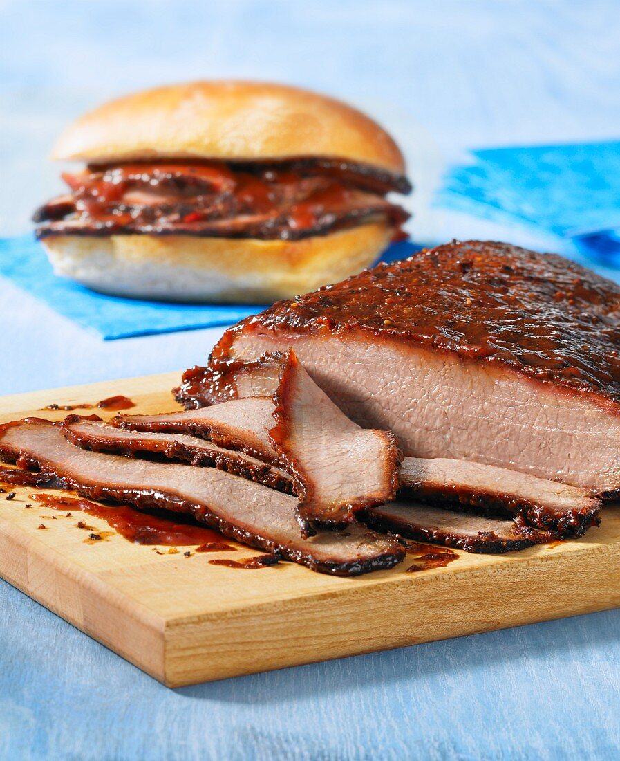 Marinierter Rinderbraten auf Schneidebrett, einige Scheiben abgeschnitten, Sandwich im Hintergrund