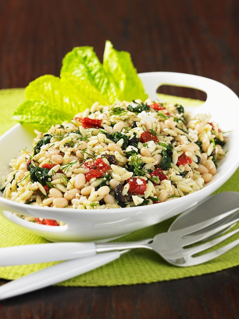 Orzo pasta with white beans, feta and vegetables in an oval dish