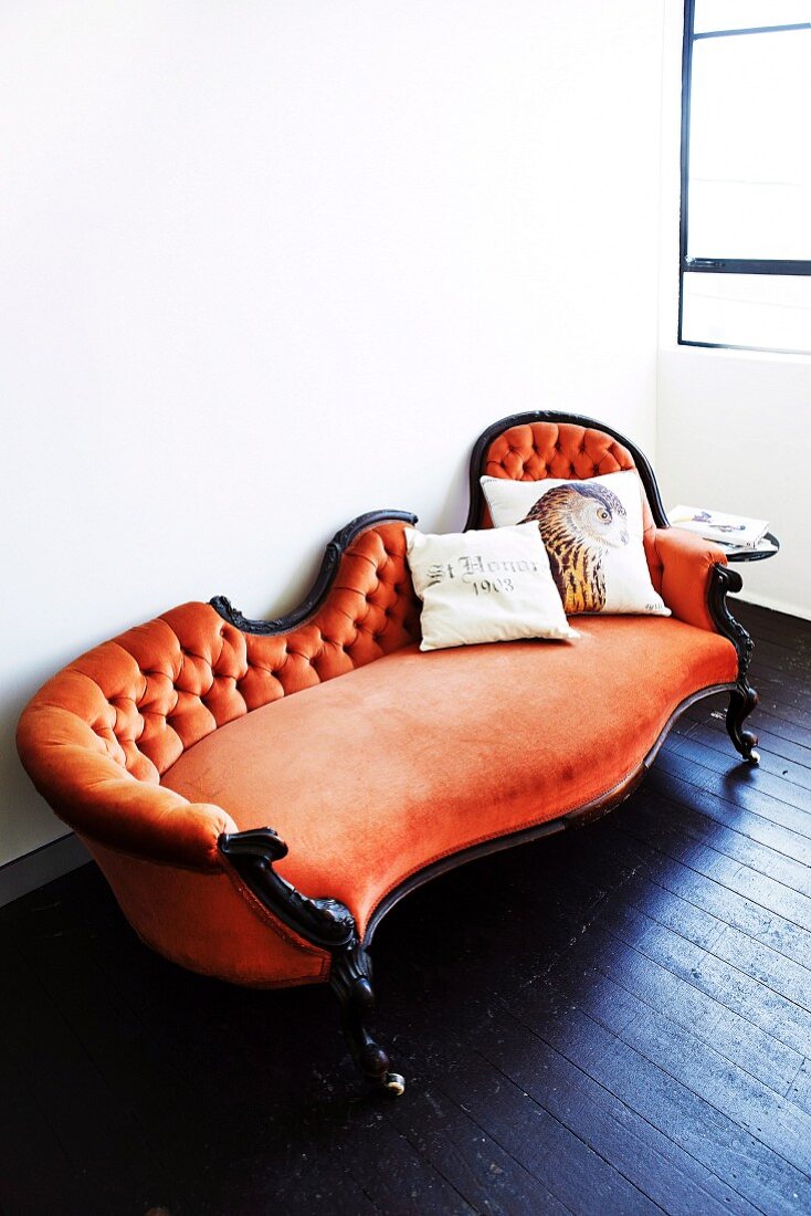 Antikes Sofa mit orangefarbenem Samtbezug und Kissen mit Vogelmotiv auf dunklem Dielenboden
