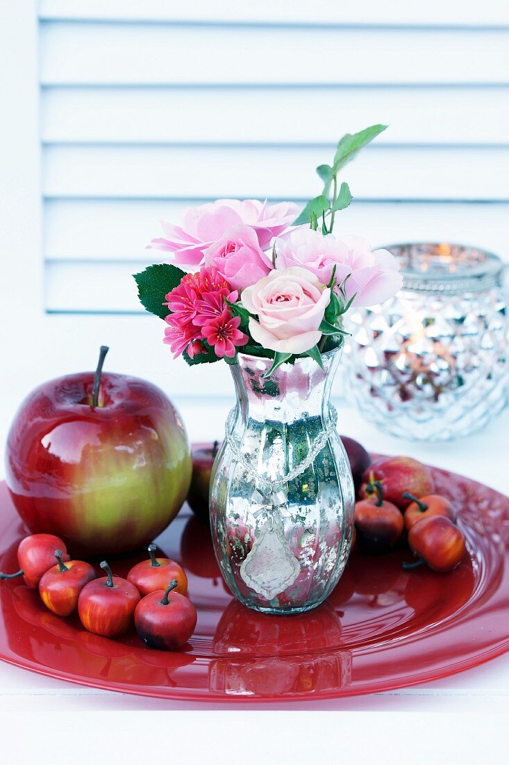 Vase in Bauernsilber-Optik mit Rosen und Dekoäpfel auf rotem Teller
