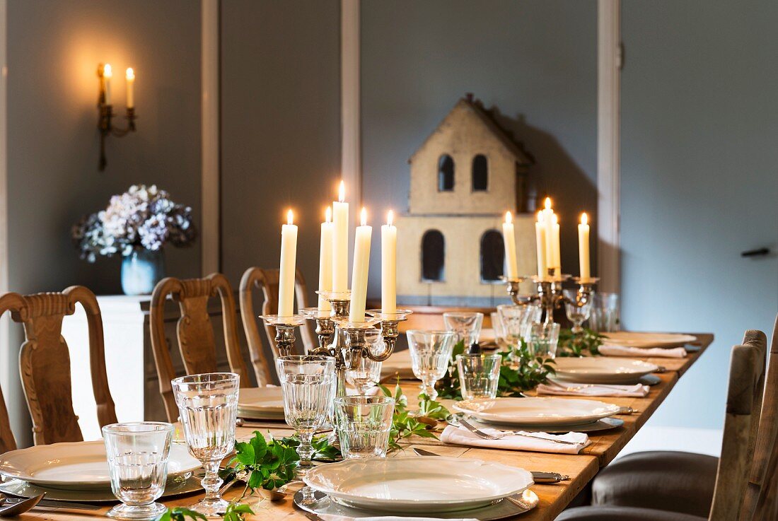 Kerzenlicht auf festlich gedeckter Tafel, im Hintergrund Modell eines Hauses