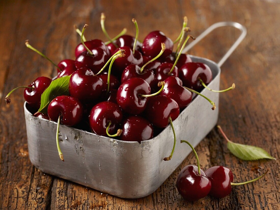 Freshly washed cherries in a metal container on a wooden surface