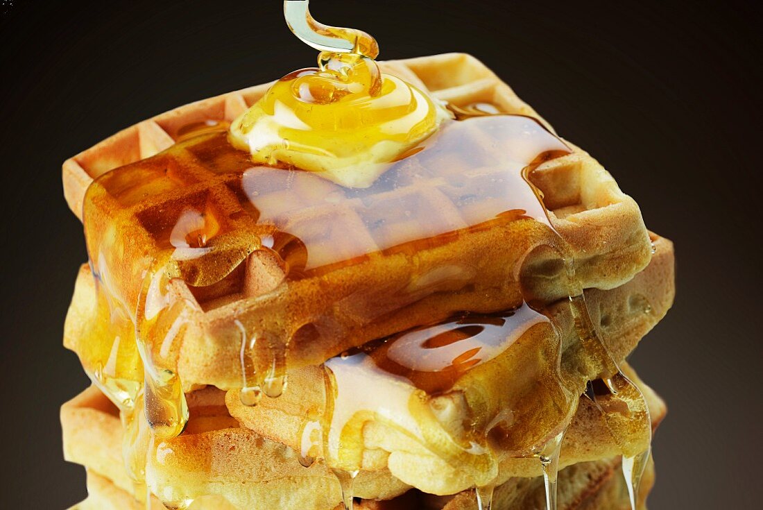 A stack of waffles with butter and dripping honey