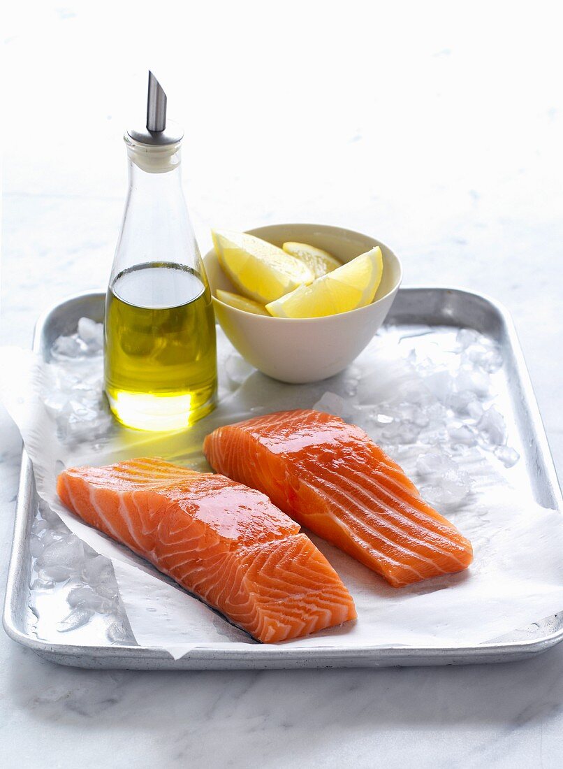 Salmon fillets on ice with olive oil and lemon wedges