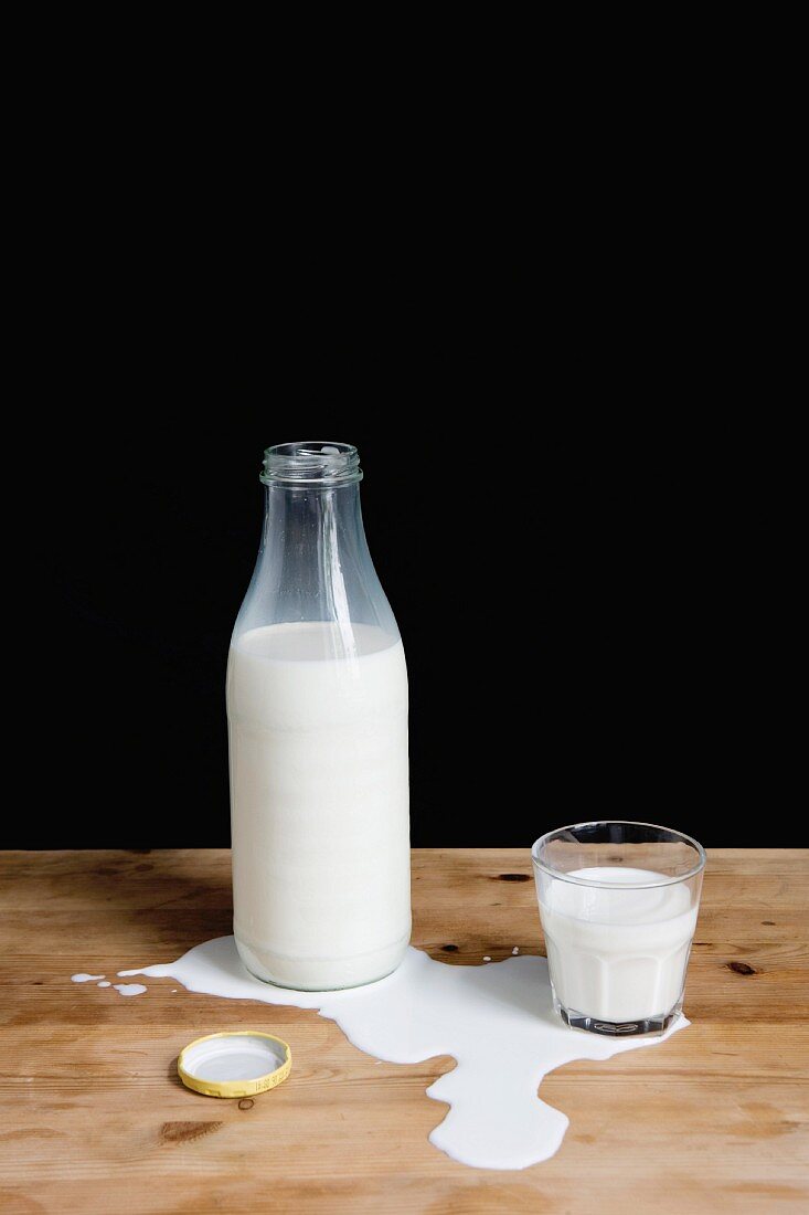 Milchflasche und Glas in einer Pfütze verschütteter Milch