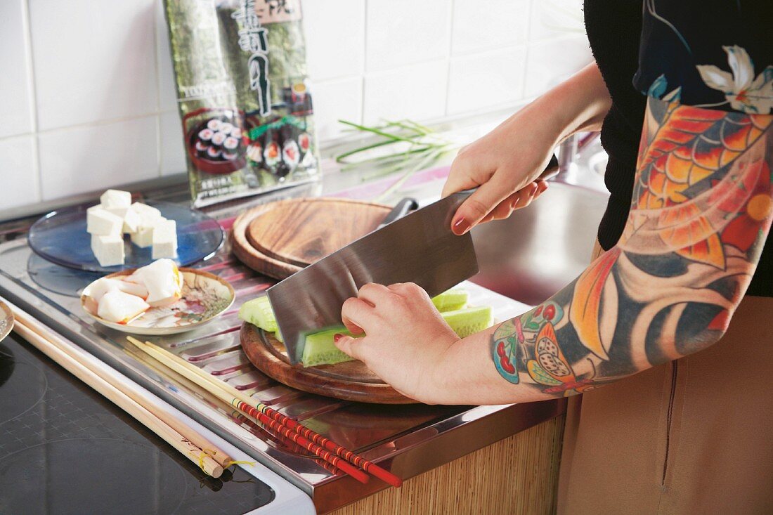 Frau mit tätowiertem Arm bereitet Sushi in der Küche vor