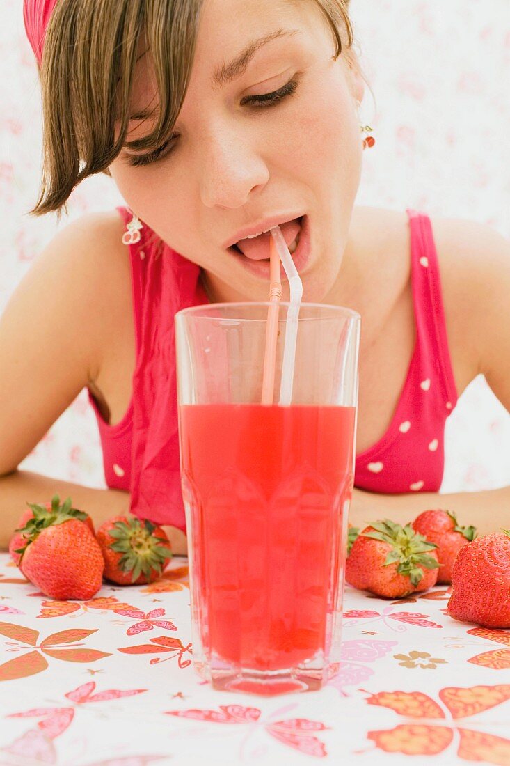 Junge Frau trinkt Erdbeerdrink mit Strohhalm