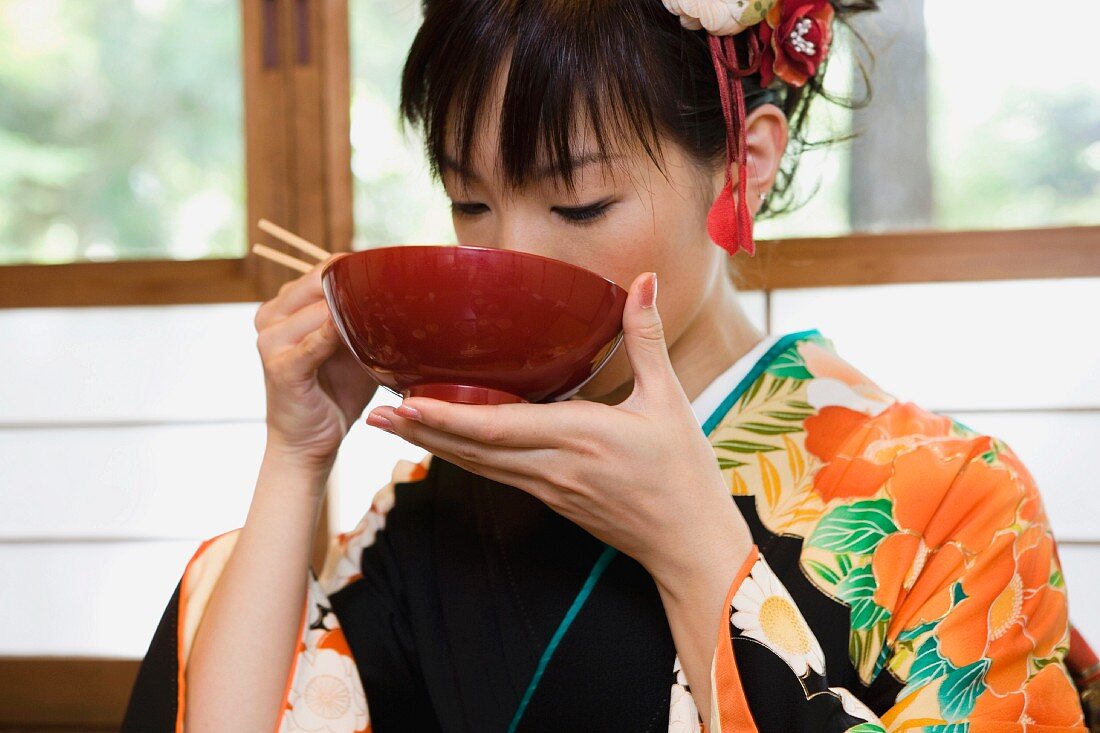 A woman wearing a kimono and eating soup