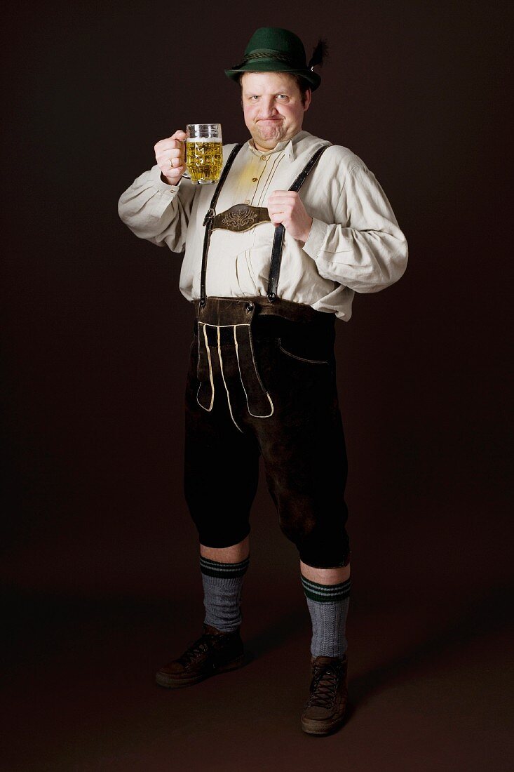 A stereotypical German man wearing lederhosen and holding a tankard of beer