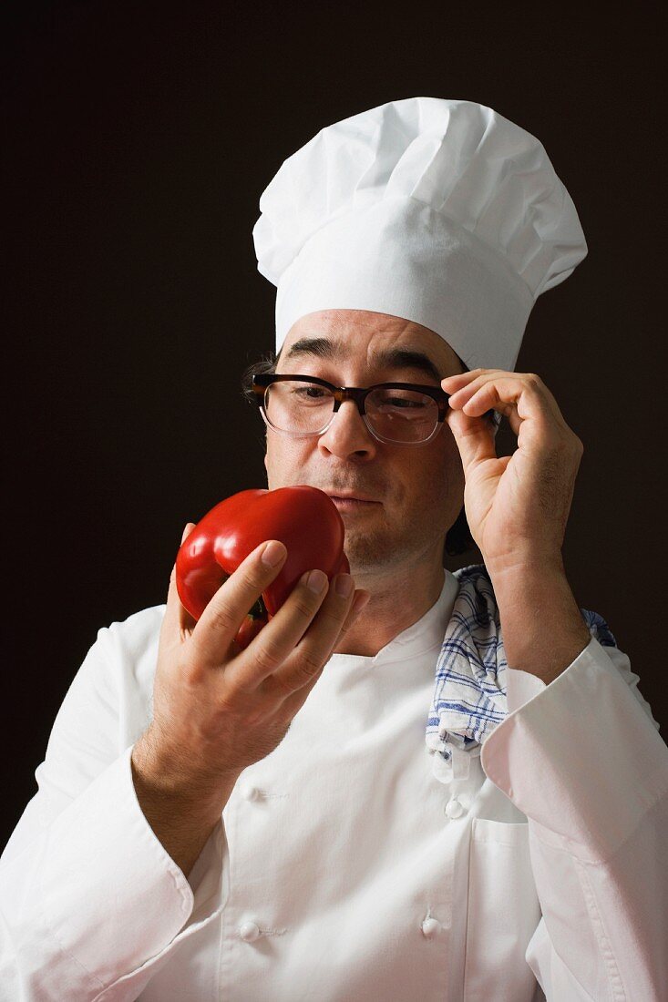 A stereotypical chef holding a red pepper