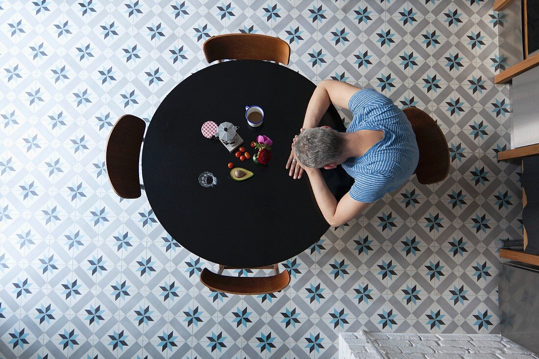 A tired man sitting at the breakfast table with his head resting on his arms